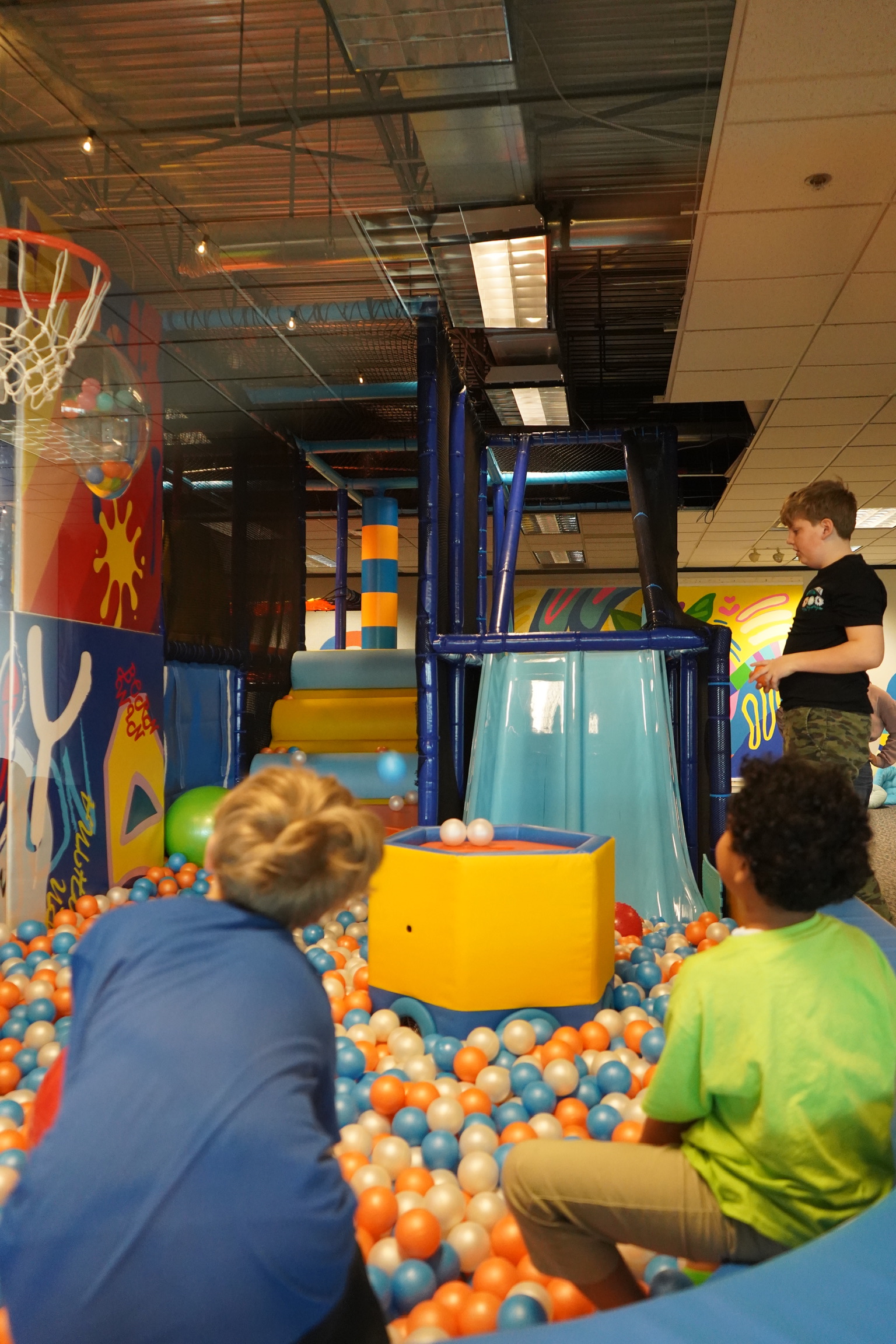 Children in indoor ball pit with blue slide and multilevel netted soft-play structure. Best playscape image; portrait.
